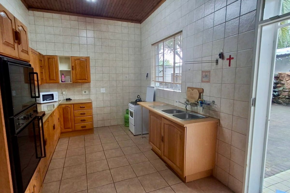 A functional kitchen featuring wooden cabinetry, tiled walls and flooring, a double sink, and a built-in oven, with direct access to the outdoor area.