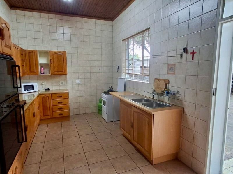 A functional kitchen featuring wooden cabinetry, tiled walls and flooring, a double sink, and a built-in oven, with direct access to the outdoor area.