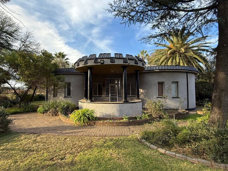 A unique circular-style home featuring a covered entrance porch with decorative columns, set within a landscaped garden with paved pathways.