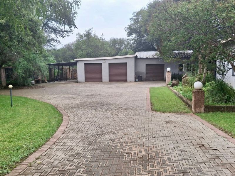 A spacious paved driveway leading to a triple garage, surrounded by established garden beds and mature trees.