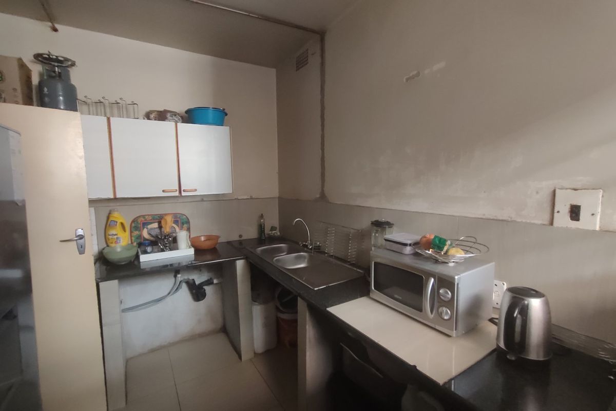 A compact kitchen area featuring built-in cabinetry, a double sink, and tiled flooring, currently requiring cosmetic updates and finishing to the wall surfaces.