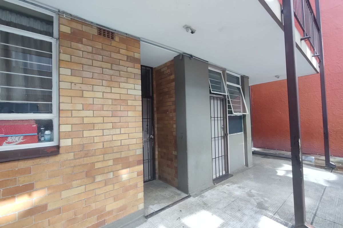 Rear exterior view of the apartment building featuring a brick facade, concrete patio area, and secure metal gated entrances.