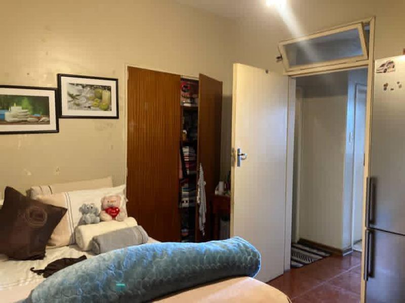 A bedroom featuring a built-in wooden wardrobe and a transom window above the doorway, showing signs of wear on the wall finishes.