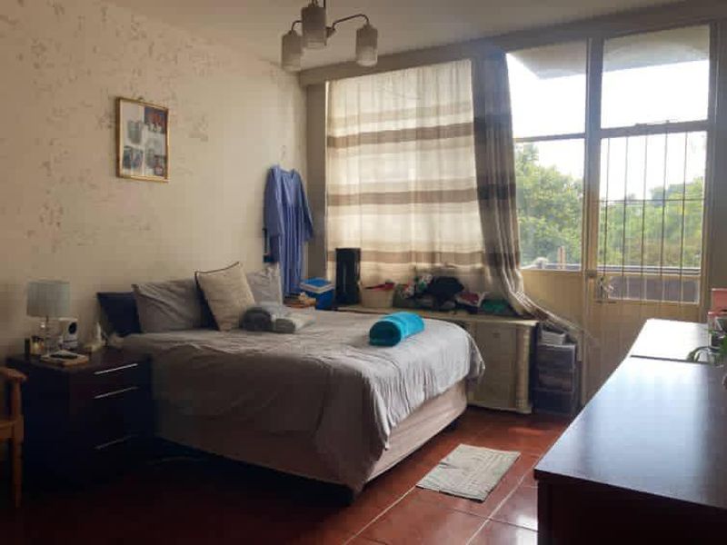 A bedroom featuring tiled flooring, large windows with access to a balcony, and significant wall surface deterioration requiring maintenance and cosmetic updates.