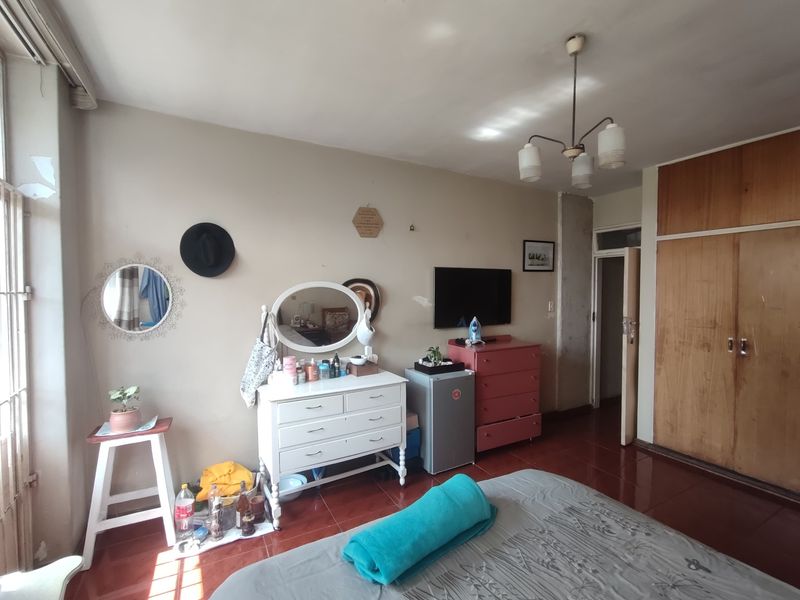 A bedroom featuring built-in wooden cupboards and tiled flooring, requiring some cosmetic attention to the wall finishes.
