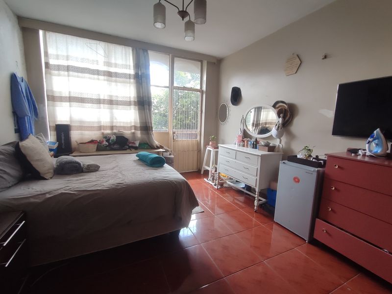 A bedroom featuring tiled flooring, a large window with natural light, and a security gate leading to an outdoor area.