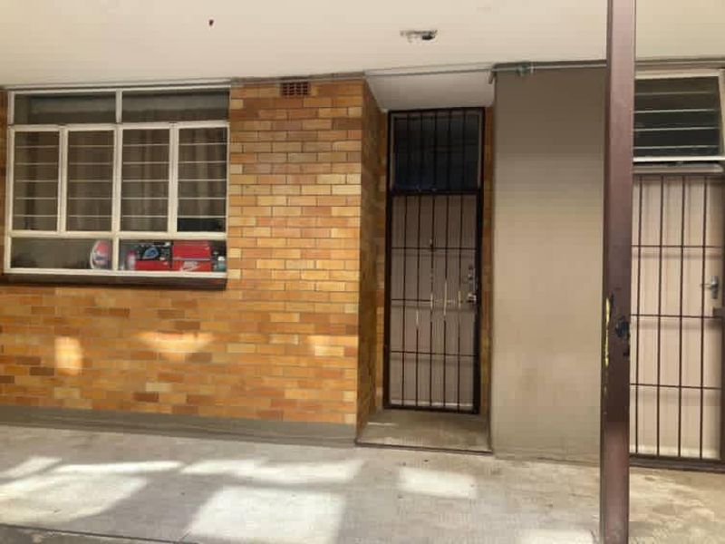 Exterior entrance area featuring a brick facade, security gate, and concrete flooring, providing access to the apartment unit.