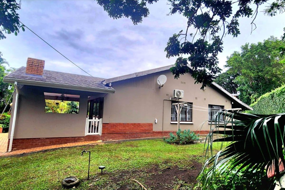 Rear view of the house featuring a brick chimney, tiled roof, and security bars on windows, set within a landscaped garden area.