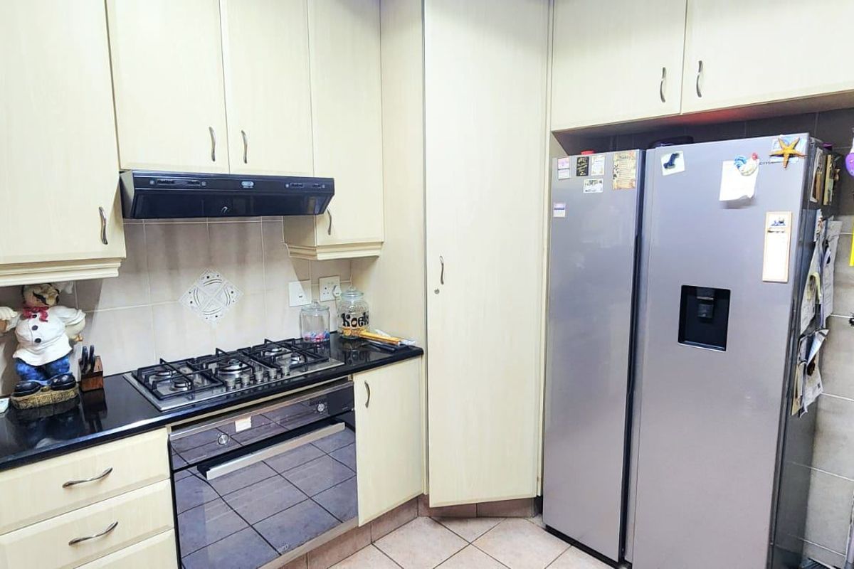 A functional kitchen featuring light-toned cabinetry, granite countertops, a gas hob with extractor fan, and tiled flooring.