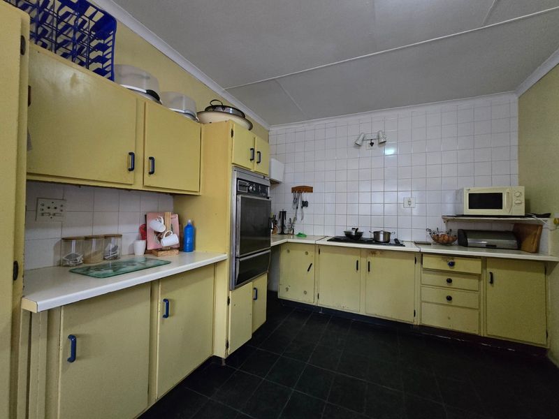 A dated kitchen featuring original yellow cabinetry, built-in oven, cooktop, and tiled backsplash, offering significant potential for a modern renovation.