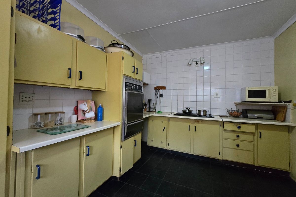 A dated kitchen featuring original yellow cabinetry, built-in oven, cooktop, and tiled backsplash, offering significant potential for a modern renovation.