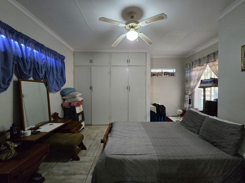 Spacious bedroom featuring built-in cupboards, tiled flooring, and a central ceiling fan, offering a functional layout with ample storage space.