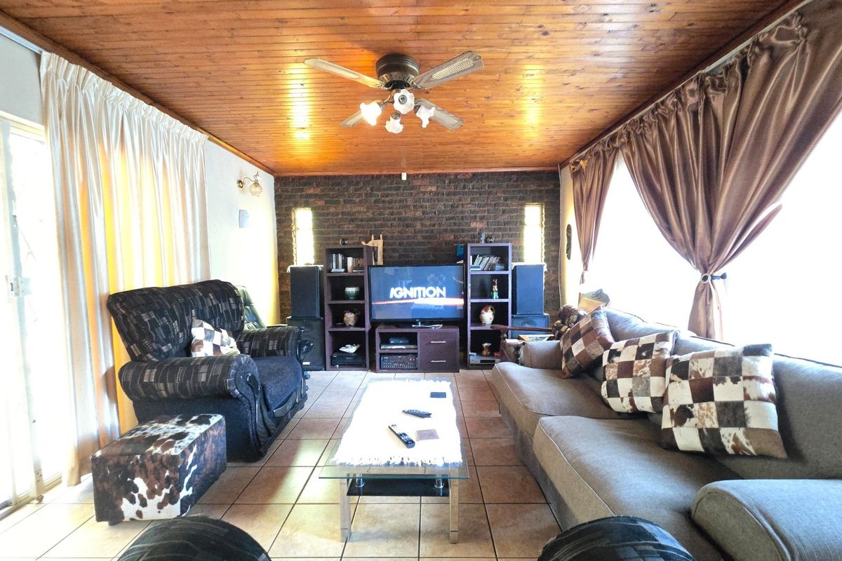 Spacious living room featuring a warm timber-clad ceiling, exposed brick feature wall, ceramic floor tiles, and direct access to the outdoors via sliding glass doors.