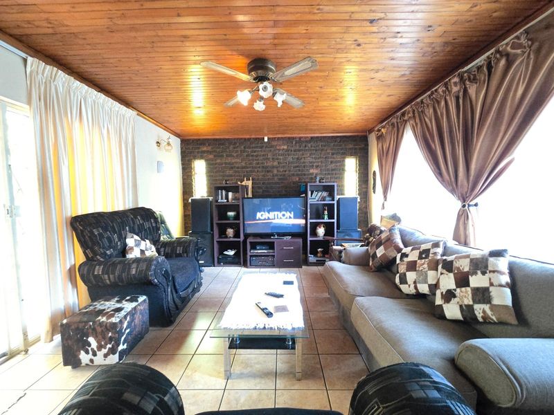Spacious living room featuring a warm timber-clad ceiling, exposed brick feature wall, ceramic floor tiles, and direct access to the outdoors via sliding glass doors.