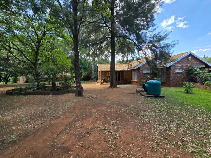 A view of the rear exterior of the brick house, featuring a large garden area with mature trees and a pool pump housing.
