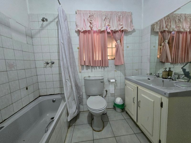 A dated bathroom featuring a bathtub, toilet, and vanity basin with tiled walls and flooring, offering potential for a modern renovation.