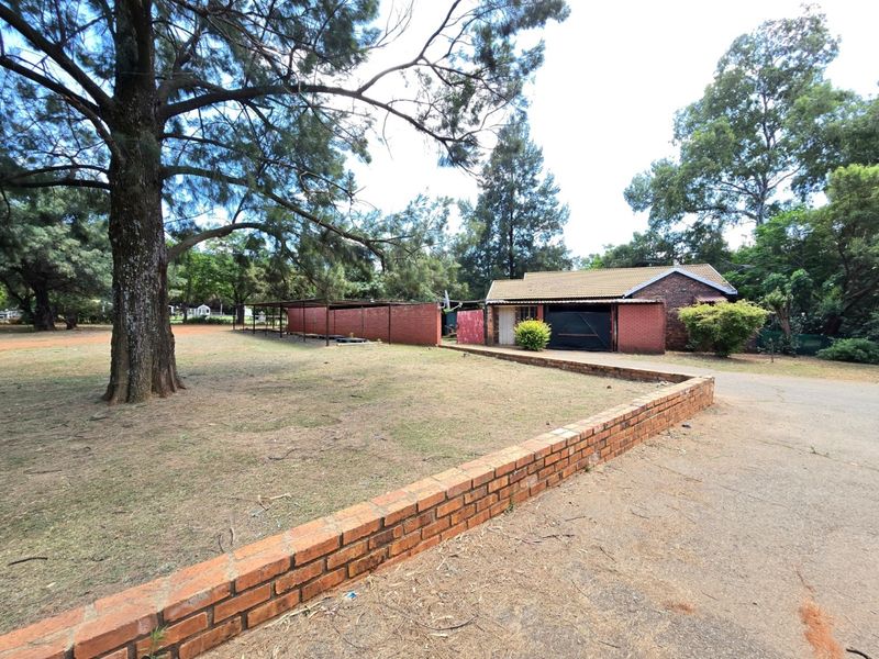 Spacious rear exterior view featuring a brick-built structure with a tiled roof, attached carport, and extensive garden area with a low brick boundary wall.
