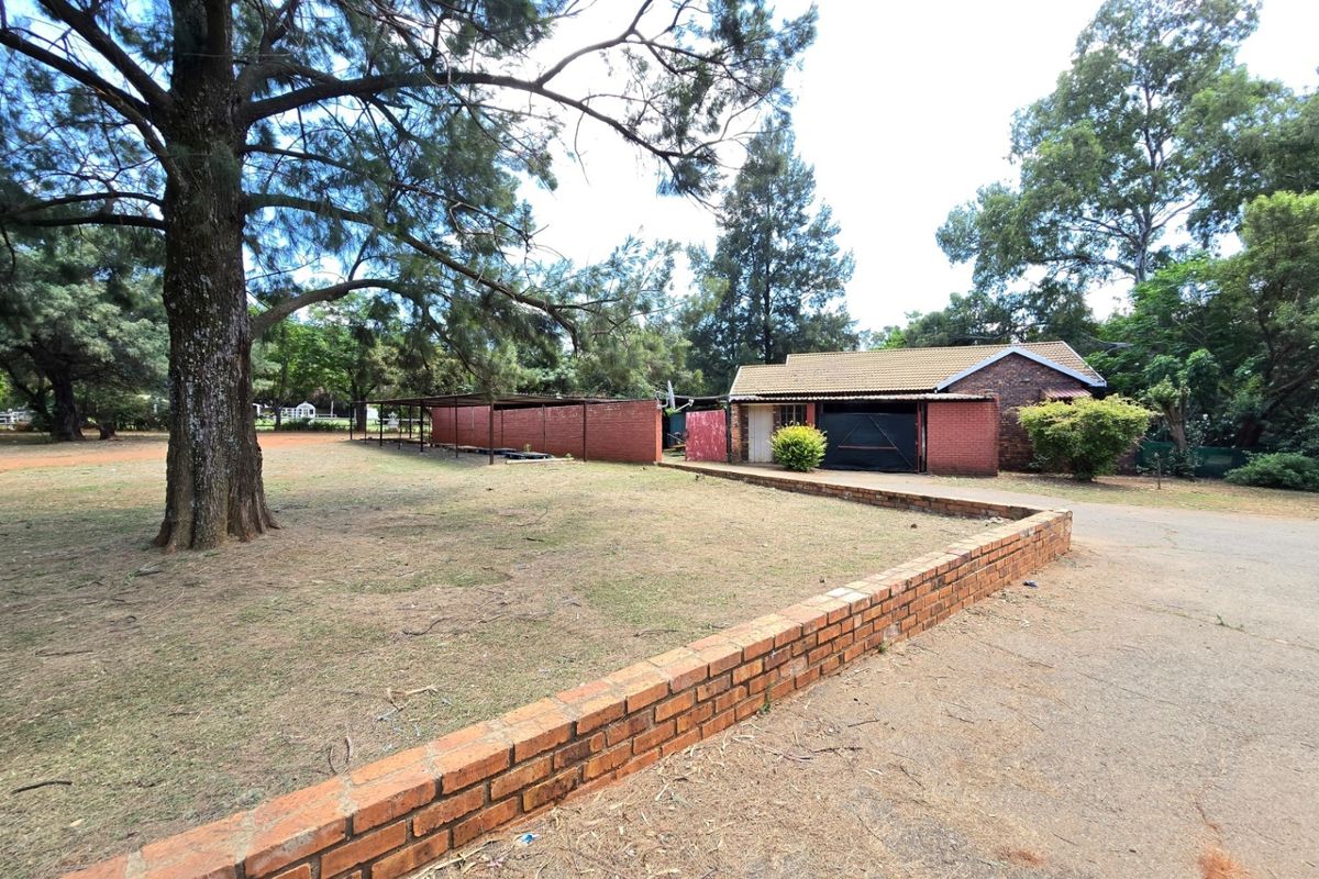 Spacious rear exterior view featuring a brick-built structure with a tiled roof, attached carport, and extensive garden area with a low brick boundary wall.
