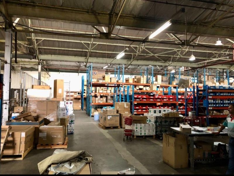 Spacious industrial warehouse featuring high-bay ceilings with exposed steel trusses, concrete flooring, and extensive integrated racking systems for storage.