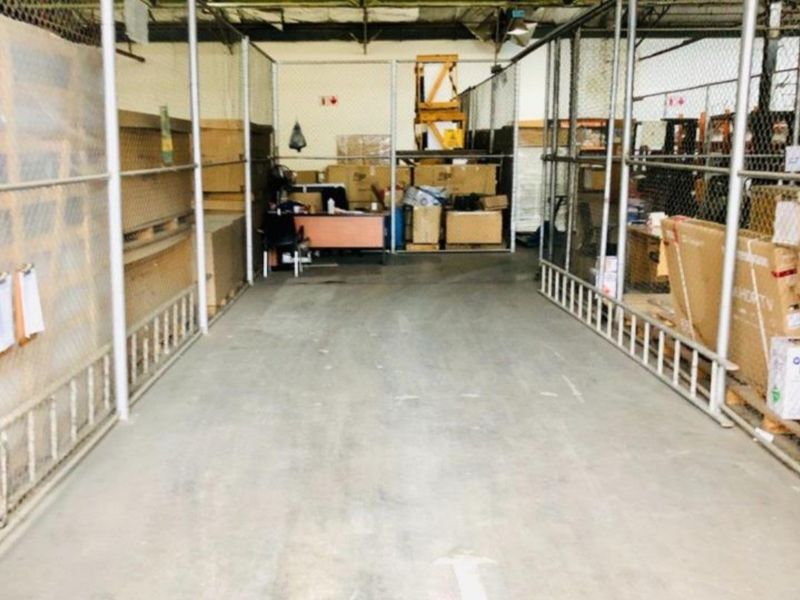Industrial warehouse utility space featuring chain-link partitioned storage areas, exposed steel roof trusses, and durable concrete flooring.