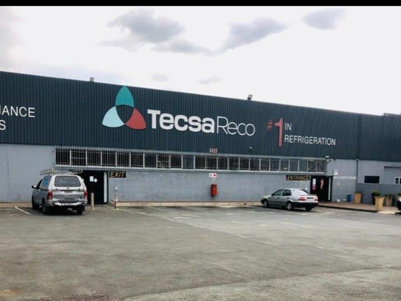 Front elevation of an industrial warehouse facility featuring metal cladding, signage, and an asphalt parking area.