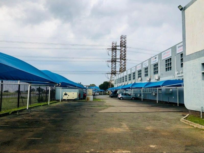 Industrial property exterior featuring an asphalt parking area with shade cloth carports and wall-mounted air conditioning units along the building facade.