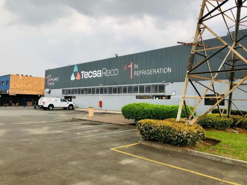 Front elevation of an industrial warehouse facility featuring metal cladding, dedicated parking area, and prominent signage.