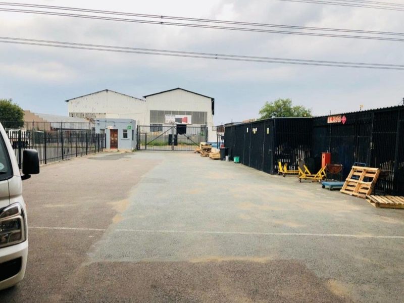 Industrial property exterior featuring a paved yard, security fencing, gated access, and a warehouse structure with a small guard house.