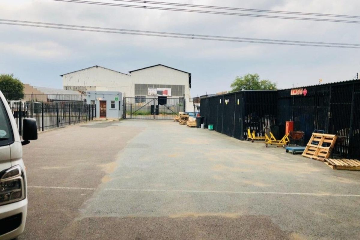 Industrial property exterior featuring a paved yard, security fencing, gated access, and a warehouse structure with a small guard house.