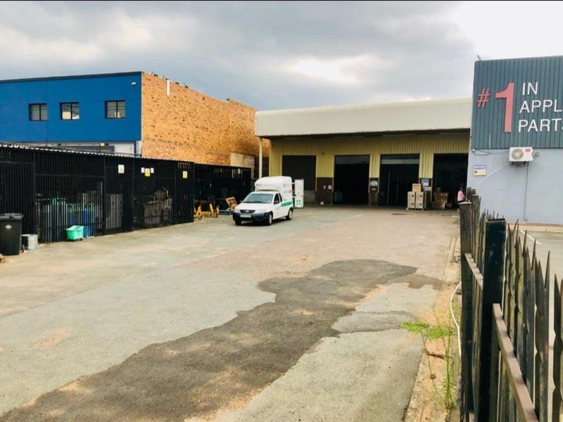 Industrial property exterior featuring a large asphalt yard, secure perimeter fencing, and multiple roller door access points for warehouse operations.