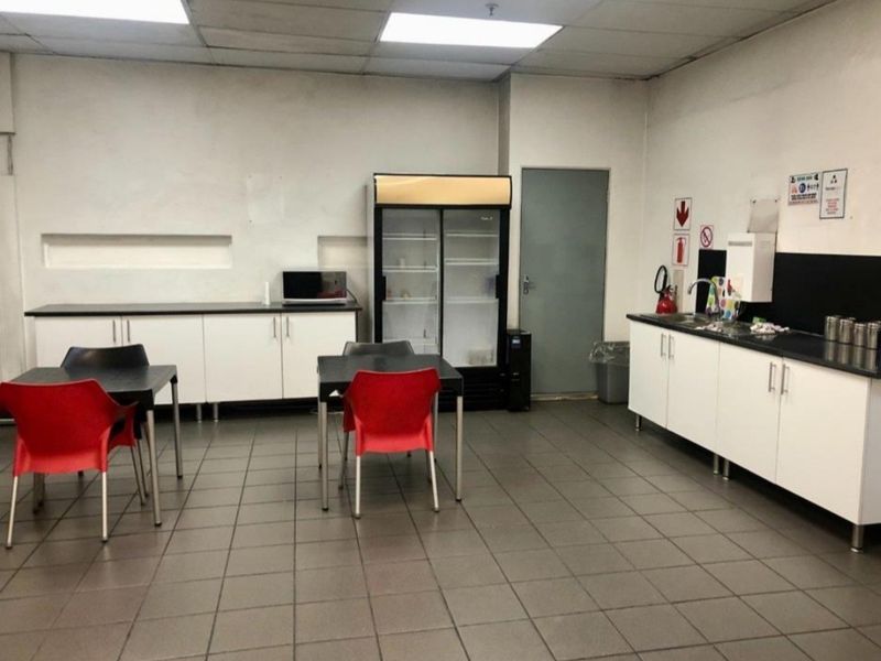 Functional industrial kitchen area featuring tiled flooring, drop ceiling, built-in cabinetry with laminate countertops, and a stainless steel sink.