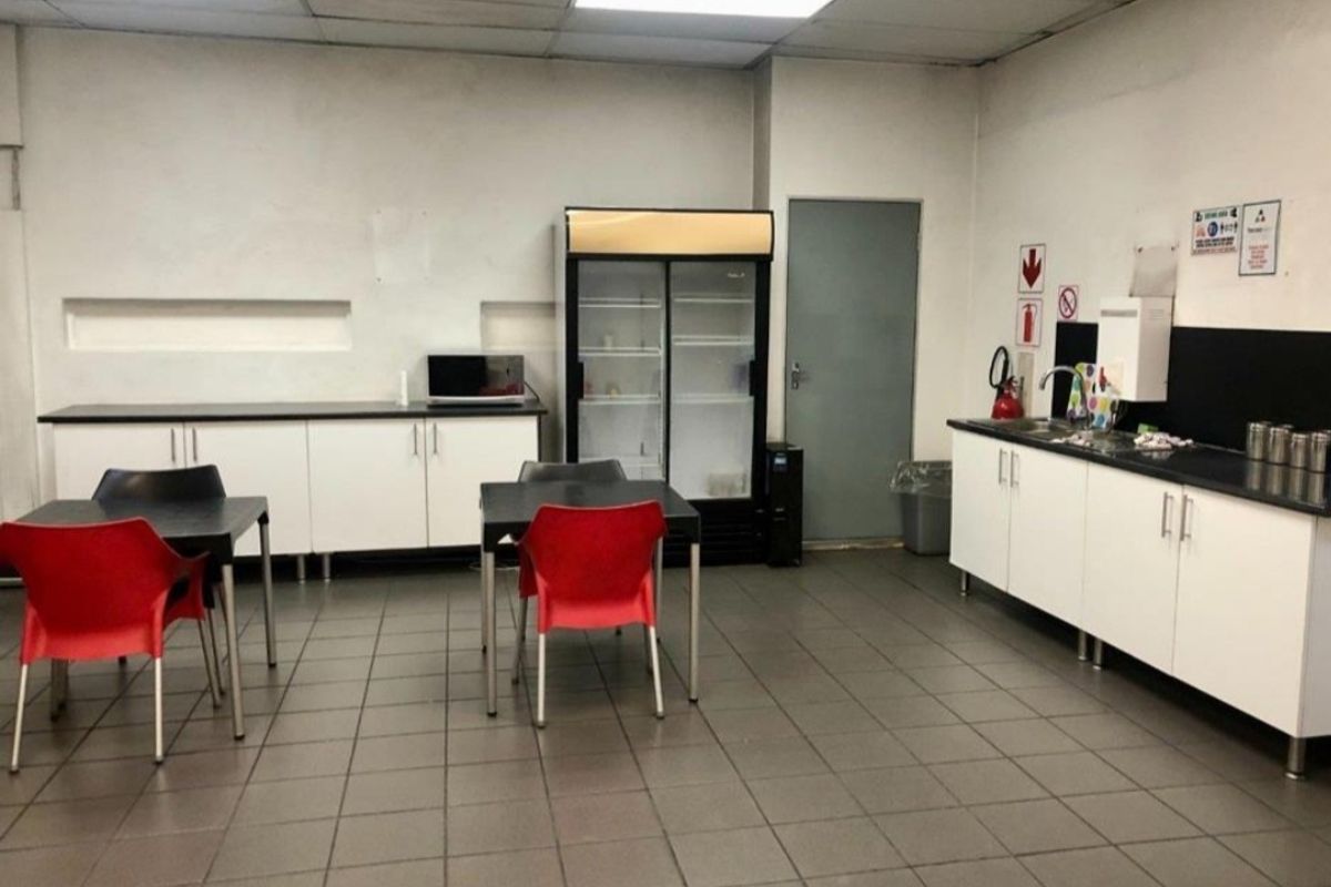 Functional industrial kitchen area featuring tiled flooring, drop ceiling, built-in cabinetry with laminate countertops, and a stainless steel sink.
