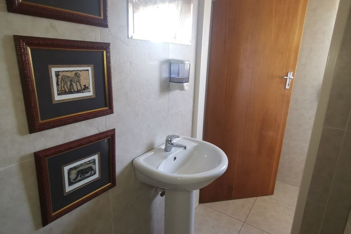 A clean, functional bathroom featuring a pedestal washbasin, chrome mixer tap, and neutral wall and floor tiling.