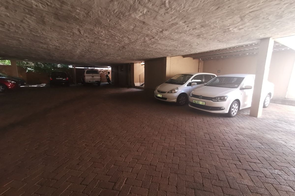 A covered parking area featuring paved flooring and structural support columns, providing sheltered vehicle storage for the commercial property.