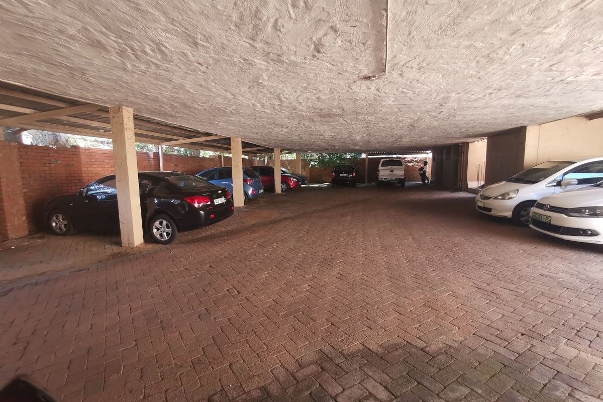 A covered commercial parking area featuring brick paving, concrete support columns, and a textured ceiling finish.
