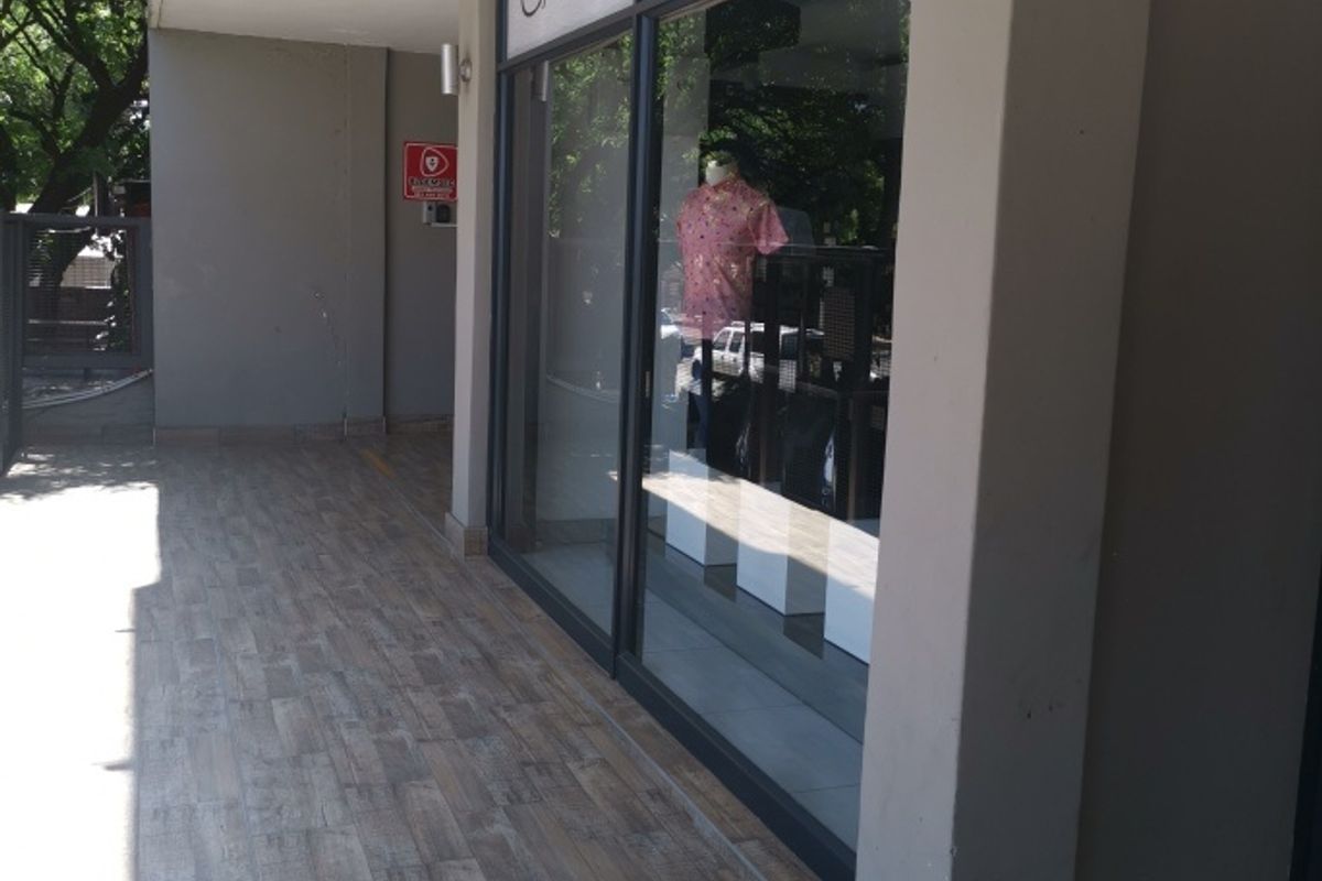 Commercial storefront entrance featuring large glass display windows, modern wood-look tiled flooring, and wall-mounted exterior lighting.