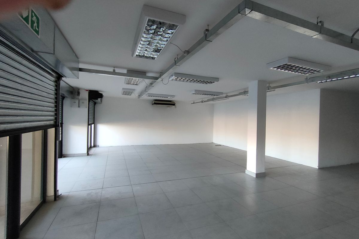 Spacious open-plan commercial unit featuring tiled flooring, roller shutter doors, exposed conduit lighting, and an integrated air conditioning unit.