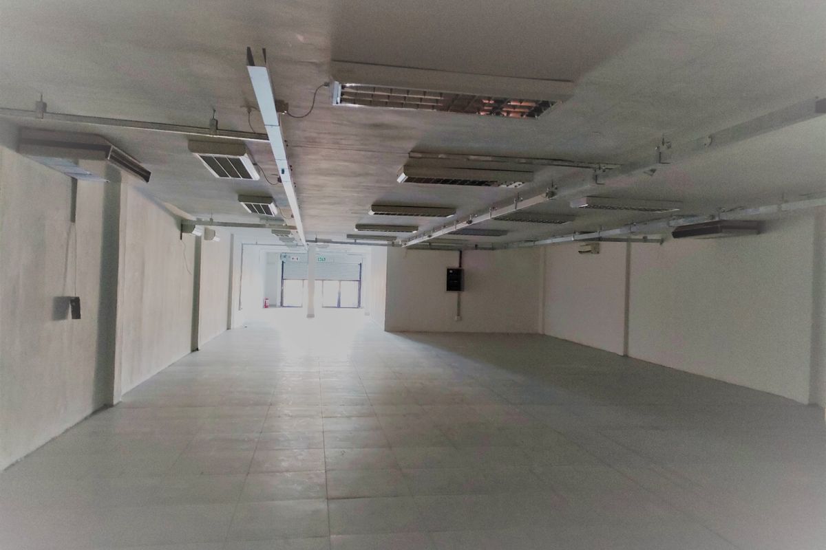 A large, vacant open-plan commercial space featuring tiled flooring, exposed lighting fixtures, and a rear roller shutter door, suitable for various business applications.