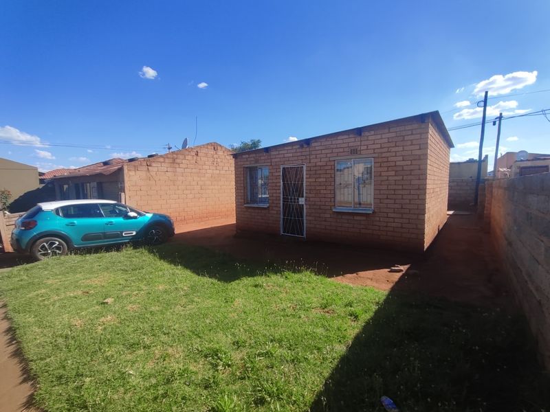 A single-story face brick residential dwelling featuring security gates and burglar bars, situated on a plot with a small lawn area.
