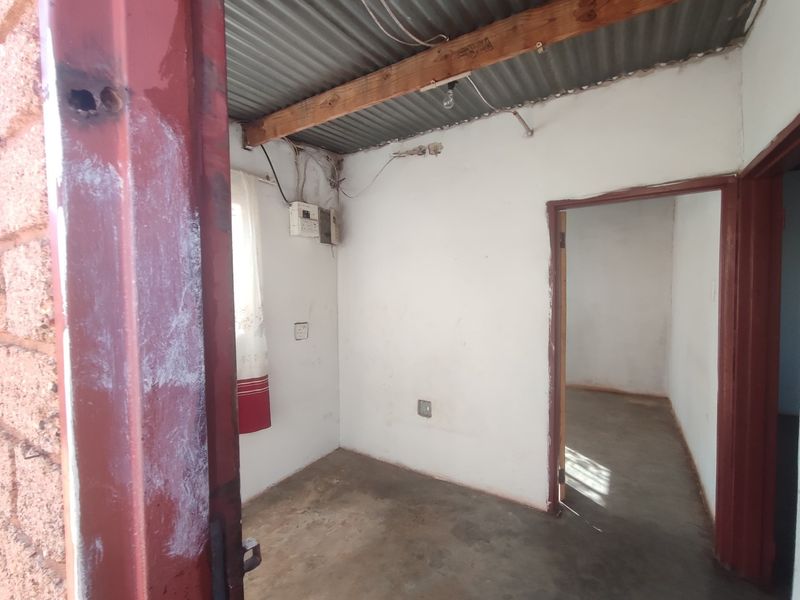 An empty, basic interior space featuring exposed corrugated metal roofing, concrete floors, and visible electrical infrastructure, offering a blank canvas for renovation.
