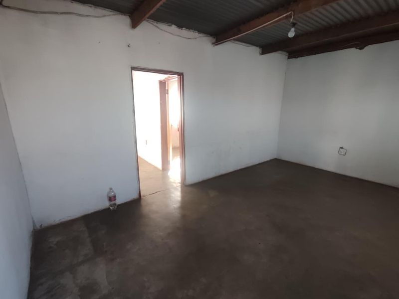 An empty, unfinished room featuring exposed timber rafters, a corrugated metal ceiling, and a concrete floor, offering a blank canvas for renovation.