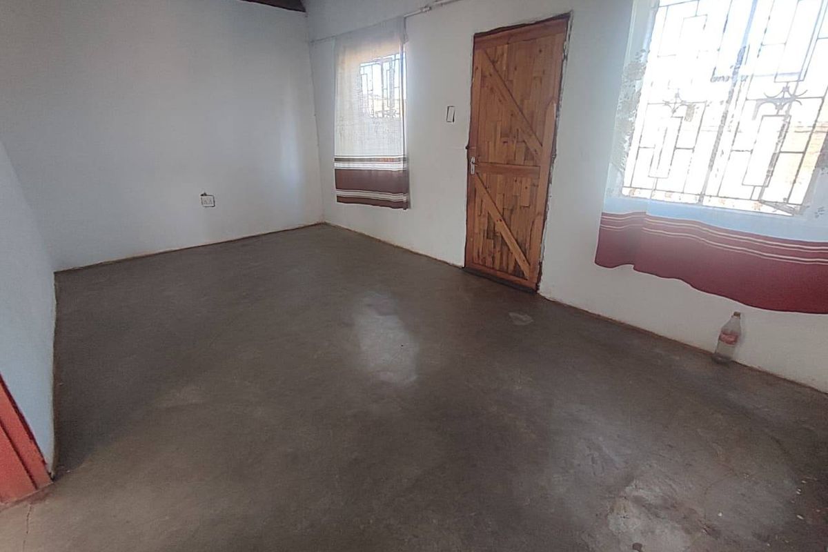 An empty bedroom featuring cement screed flooring, exposed timber ceiling beams, and security bars on the windows.