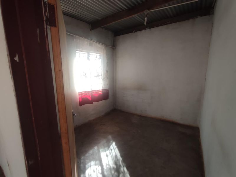 A small, basic bedroom featuring a concrete floor and exposed corrugated iron ceiling, presenting a blank canvas for renovation.