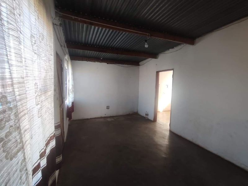 An empty living area featuring a corrugated iron ceiling with exposed timber beams and a concrete floor.