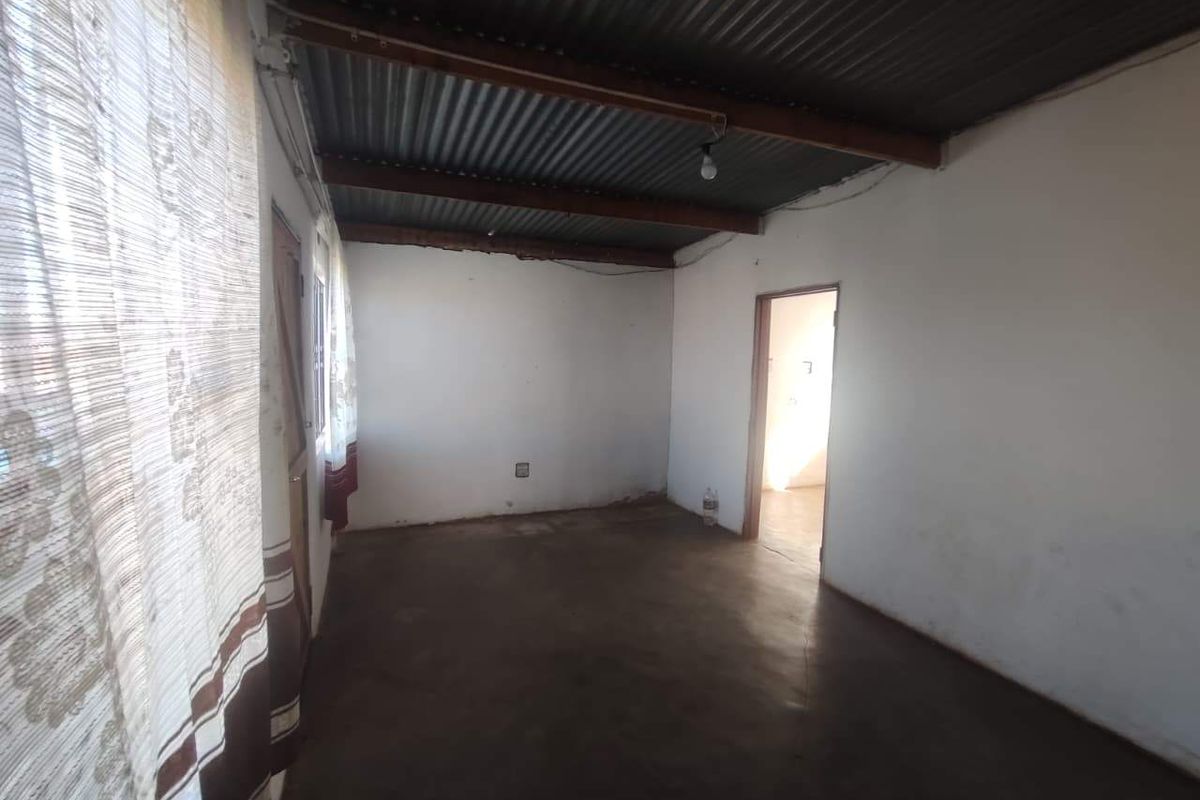 An empty living area featuring a corrugated iron ceiling with exposed timber beams and a concrete floor.