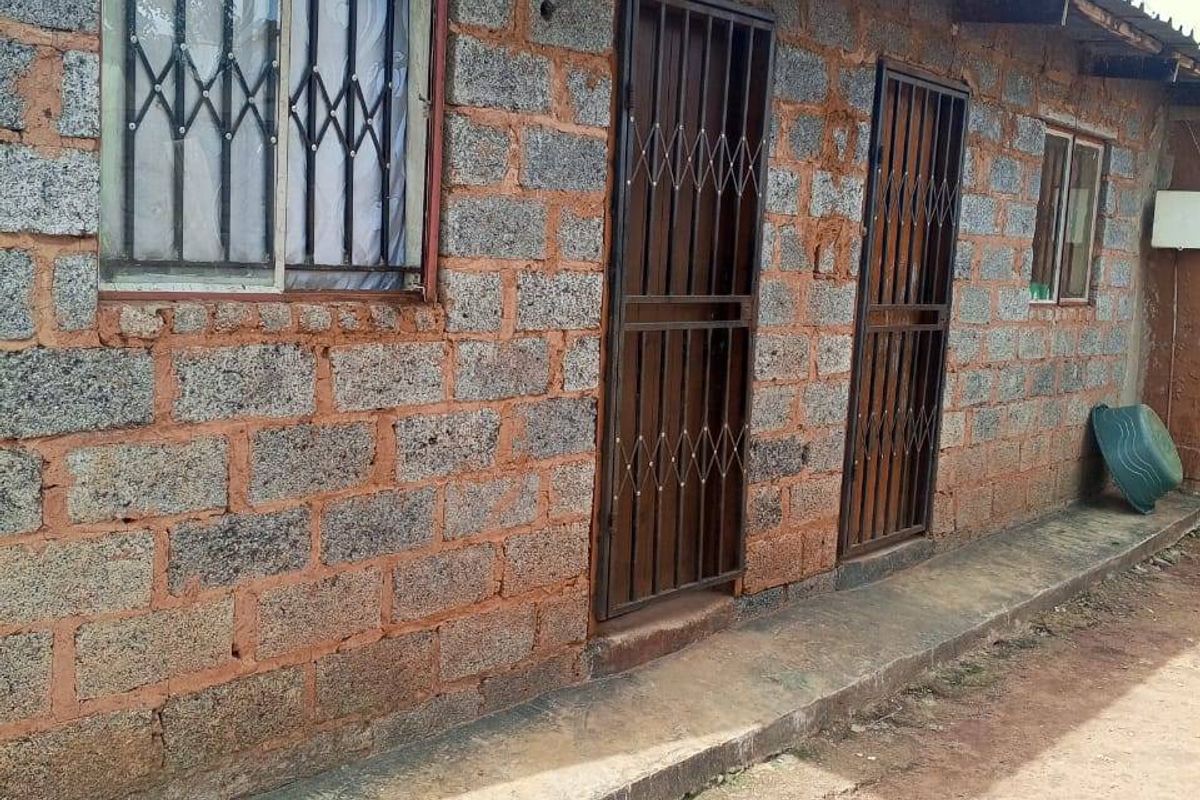 Exterior view of a concrete block structure featuring security gates, window bars, and a corrugated metal roof with a cracked concrete apron.