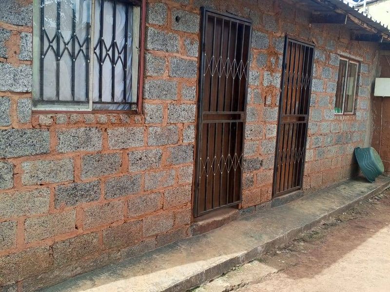 Exterior view of a concrete block structure featuring security gates, window bars, and a corrugated metal roof with a cracked concrete apron.