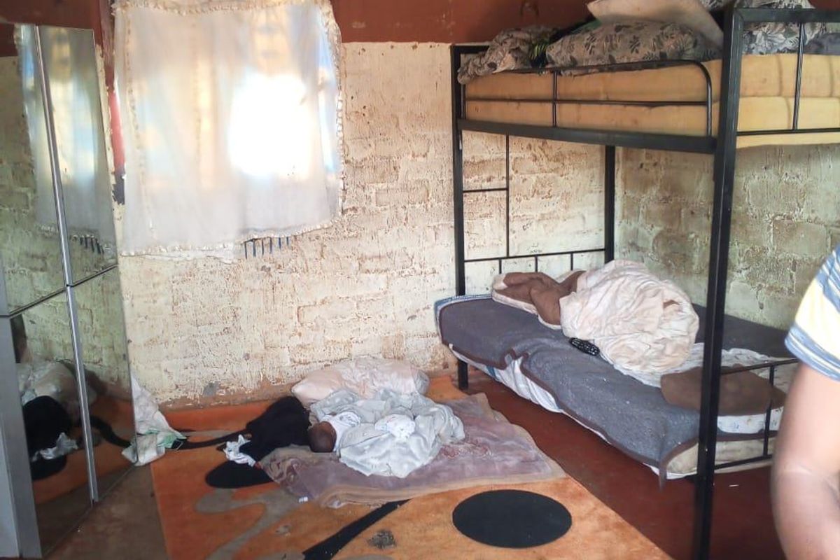 A basic bedroom featuring exposed brick walls, a corrugated metal roof, and a concrete floor, requiring significant renovation to improve finishes.