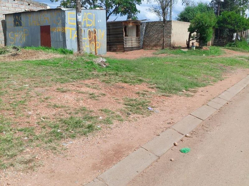 Street view showing unpaved verge and basic corrugated iron structures in a residential area.