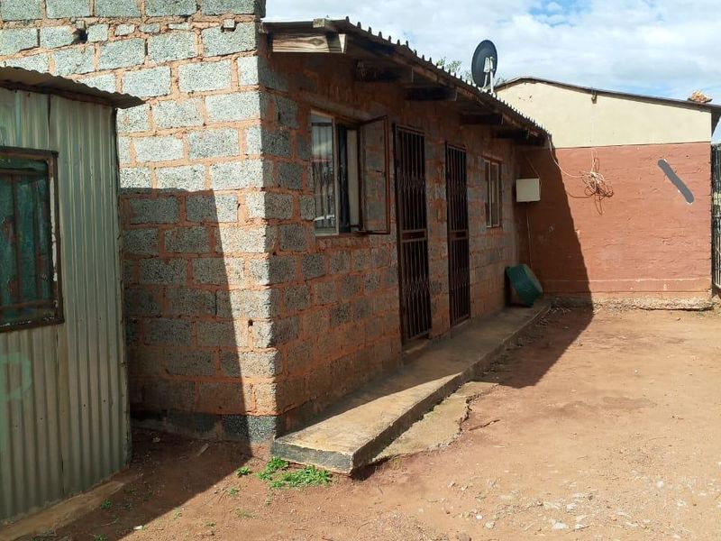 Rear view of a single-story dwelling featuring unfinished concrete block walls, corrugated metal roofing, and security gates on the entrance doors.